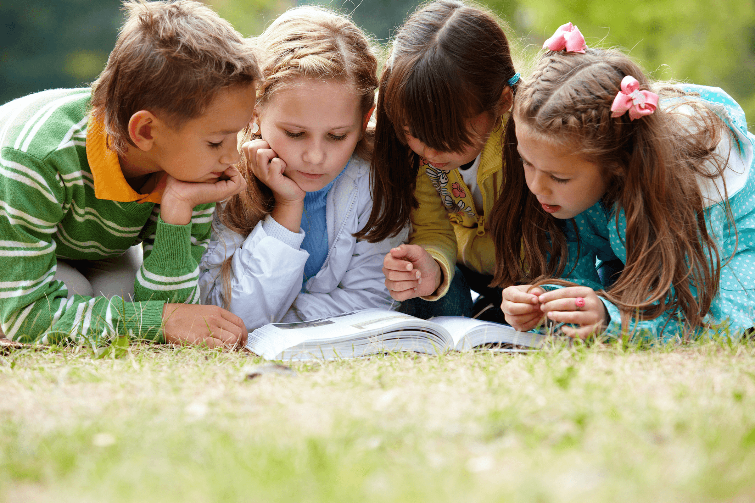 4 kids reading a book outside in the grass