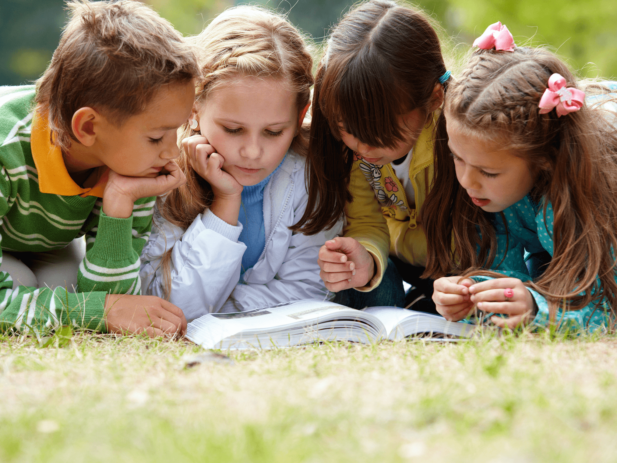 4 kids reading a book outside in the grass